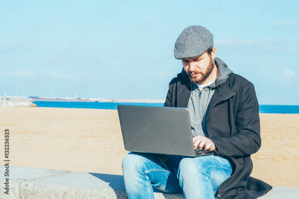 Man using laptop computer outside on the coast.