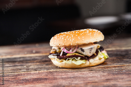 Tasty grilled beef burger with lettuce, ketchup, onion rings, chili and mayonnaise served on pieces of brown paper on a rustic wooden table of counter, with copyspace
