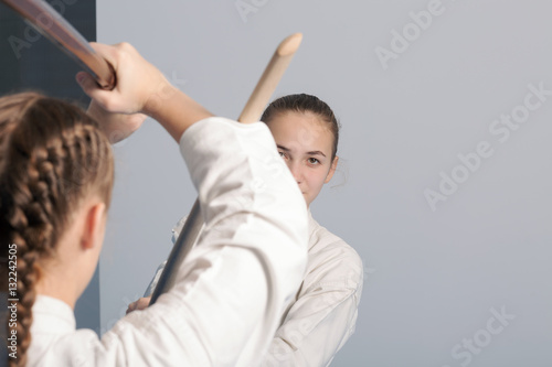 Two girls practice sword on Aikido training on white background. Selective focus