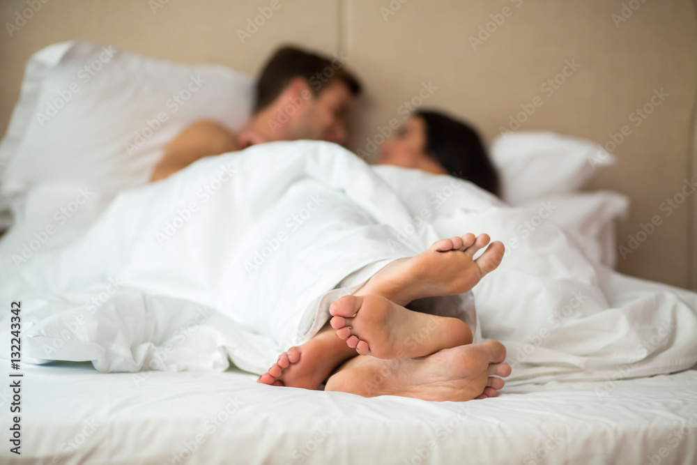 Couple's feet in bed. Man with woman under blanket. Rest in home comfort. Couple's feet in bed. Man with woman under blanket. Rest in home comfort.