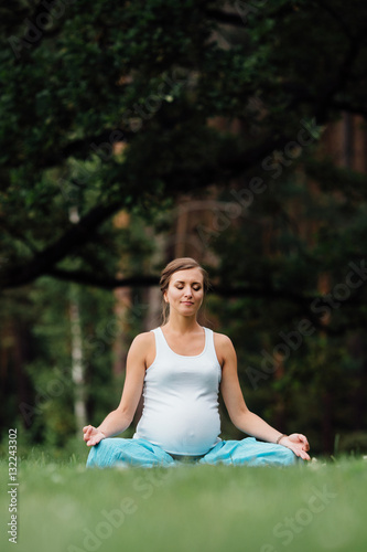 pregnant yoga in the lotus position on the forest background. in the park the grass mat, outdoor, health woman.