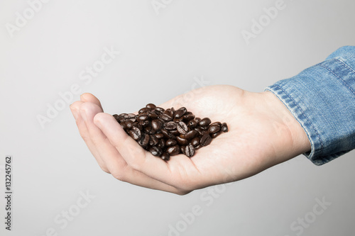 Hand in blue shirt is holding coffee beans