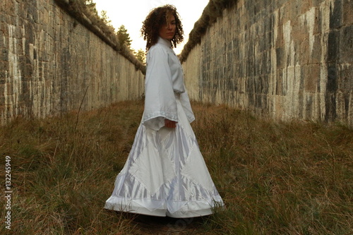 Mujer con traje blanco en la naturaleza, atrapada entre muros
