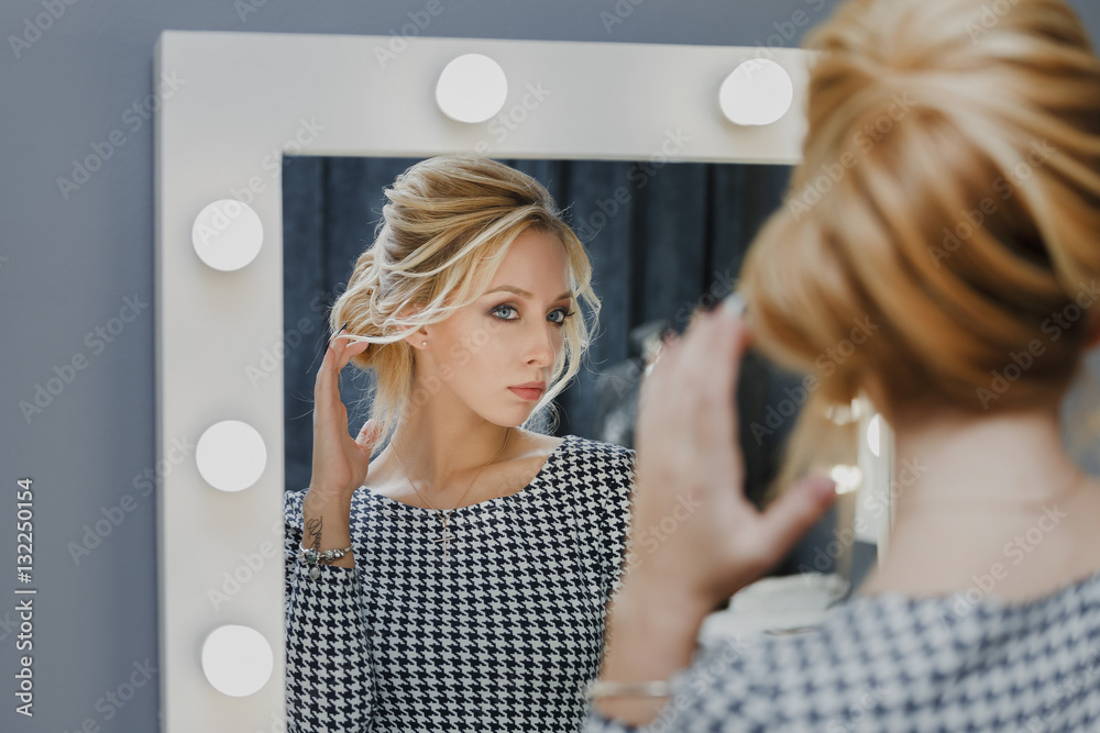 Φωτογραφία Woman in a beauty salon looks at her reflection in the mirror with lamps and che
