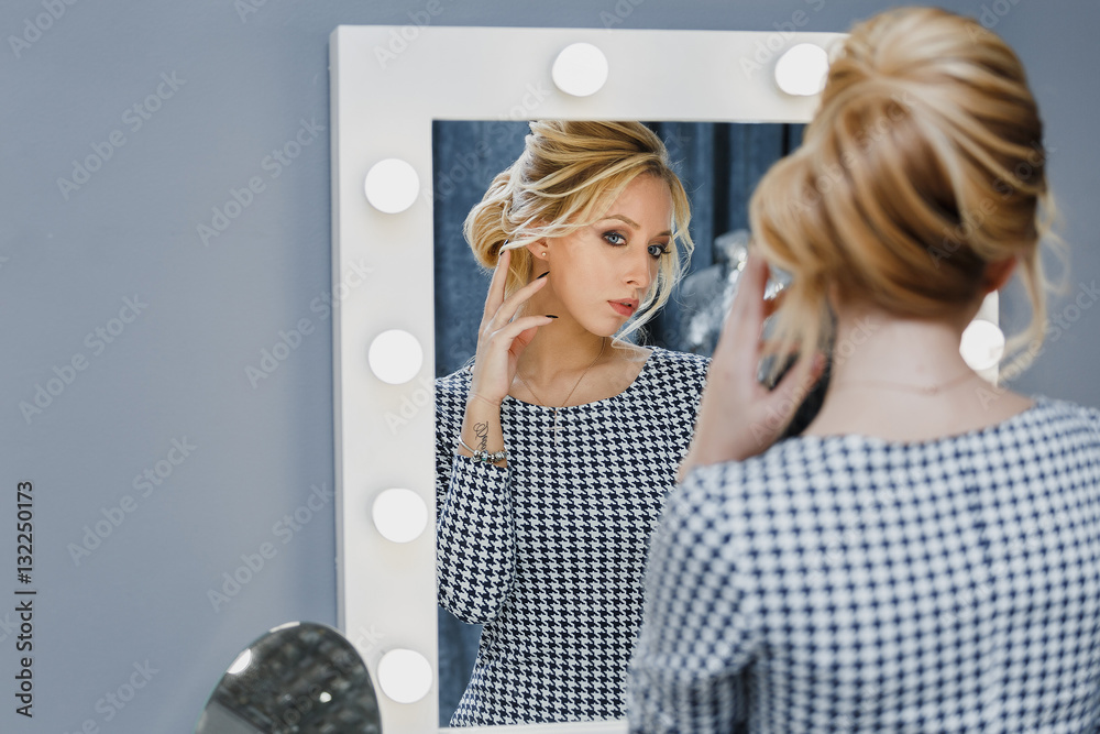 Φωτογραφία Woman in a beauty salon looks at her reflection in the mirror with lamps and che