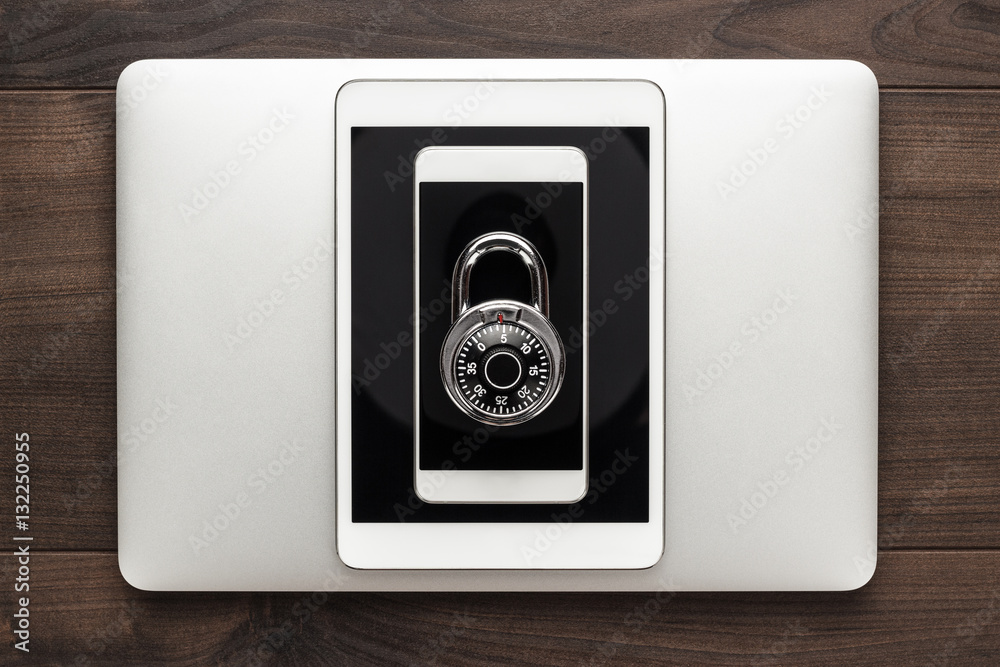 data security concept: computer, tablet, phone with combination lock on wooden table data security concept: computer, tablet, phone with combination lock on wooden table