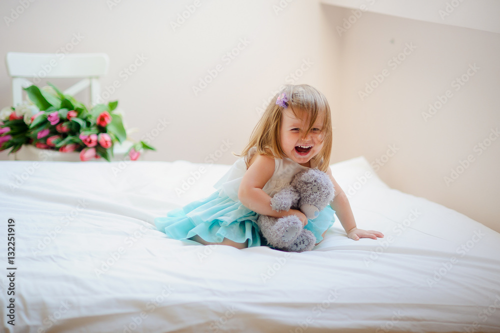 The charming little girl sits on a big bed.