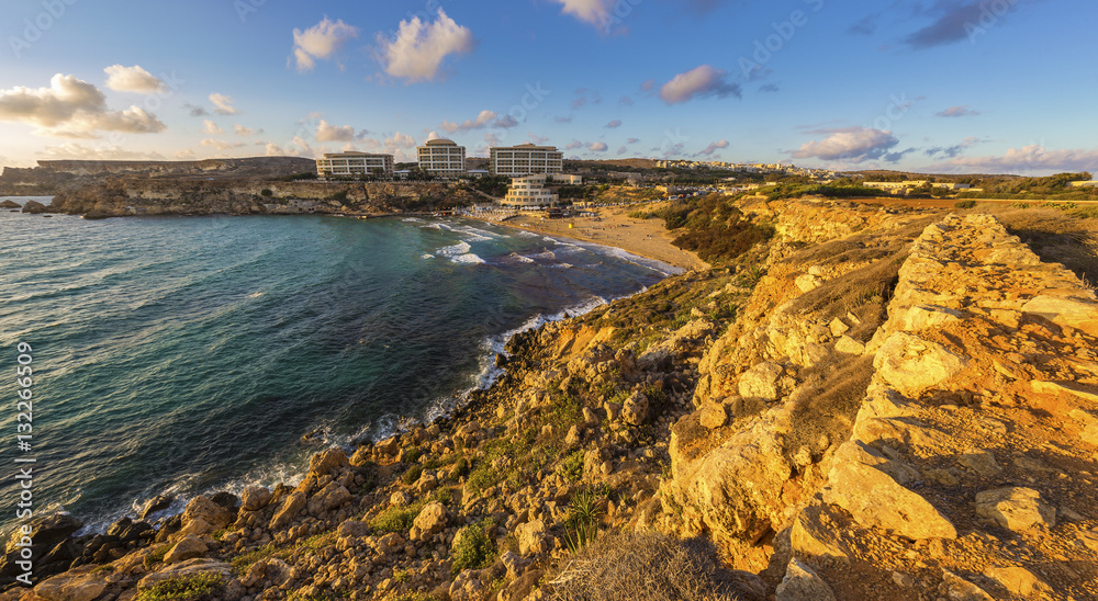 Ghajn Tuffieha, Malta - Panoramic skyline view of Golden Bay, Malta's most beautiful sandy beach at sunset with blue sky and clouds