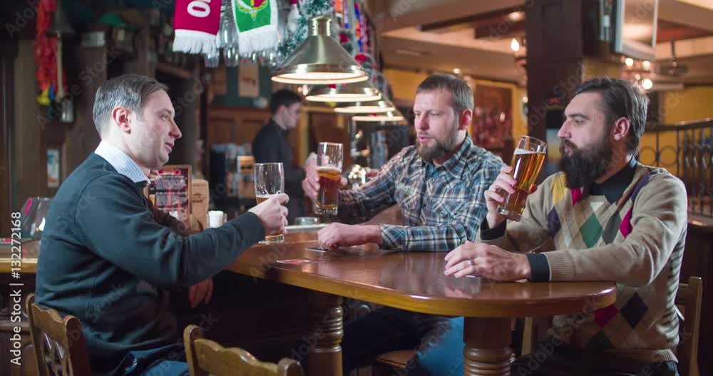 Friends group talks and drinks beer at pub bar 4k video. Men taste lager from glasses, bartender at the background. Friends group talks and drinks beer at pub bar 4k video. Men taste lager from glasses, bartender at the background.