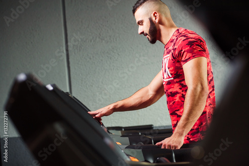 Smiling man choosing program while exercising on treadmill in gy