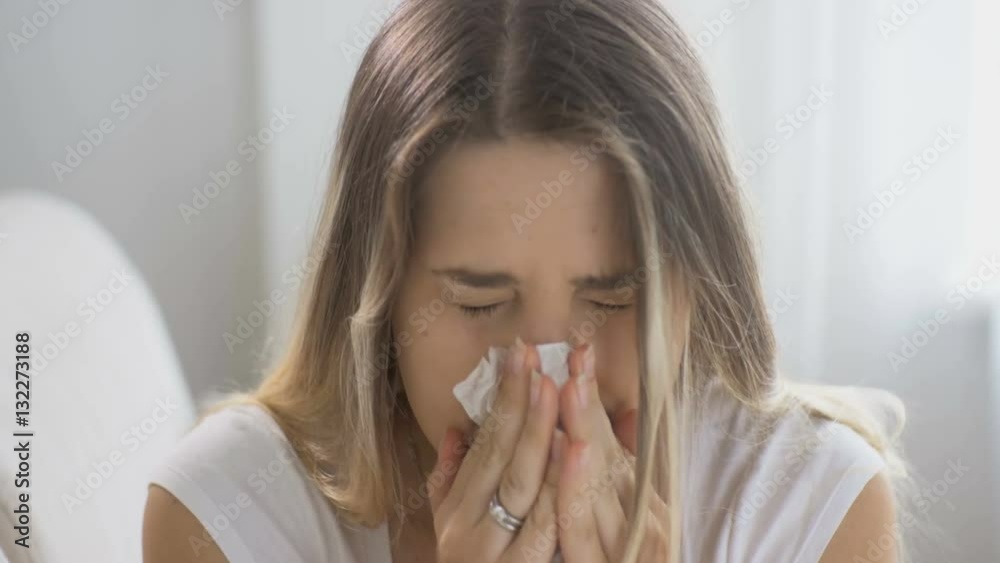 Closeup of young woman with flu sneezing in paper tissue. Footage shot in 4k definition Closeup of young woman with flu sneezing in paper tissue. Footage shot in 4k definition