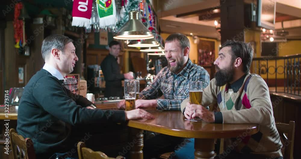Male friends talks and drinks beer at pub bar HD slow-motion video. Men speaking, laughing and smiling, having fun. Bartender at the background. Male friends talks and drinks beer at pub bar HD slow-motion video. Men speaking, laughing and smiling, having fun. Bartender at the background.