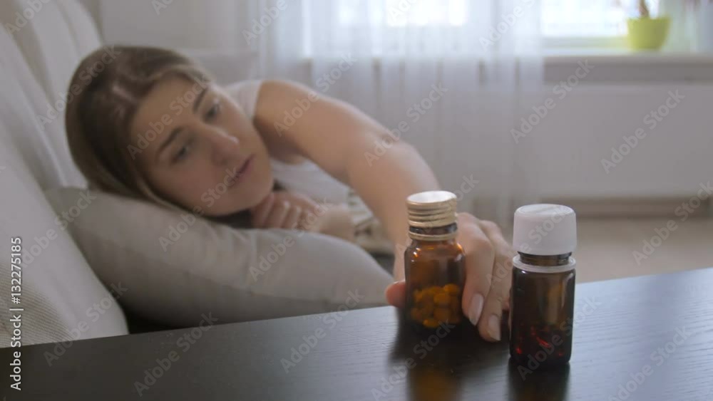 Young coughing woman lying on sofa taking pills from bedside table Young coughing woman lying on sofa taking pills from bedside table