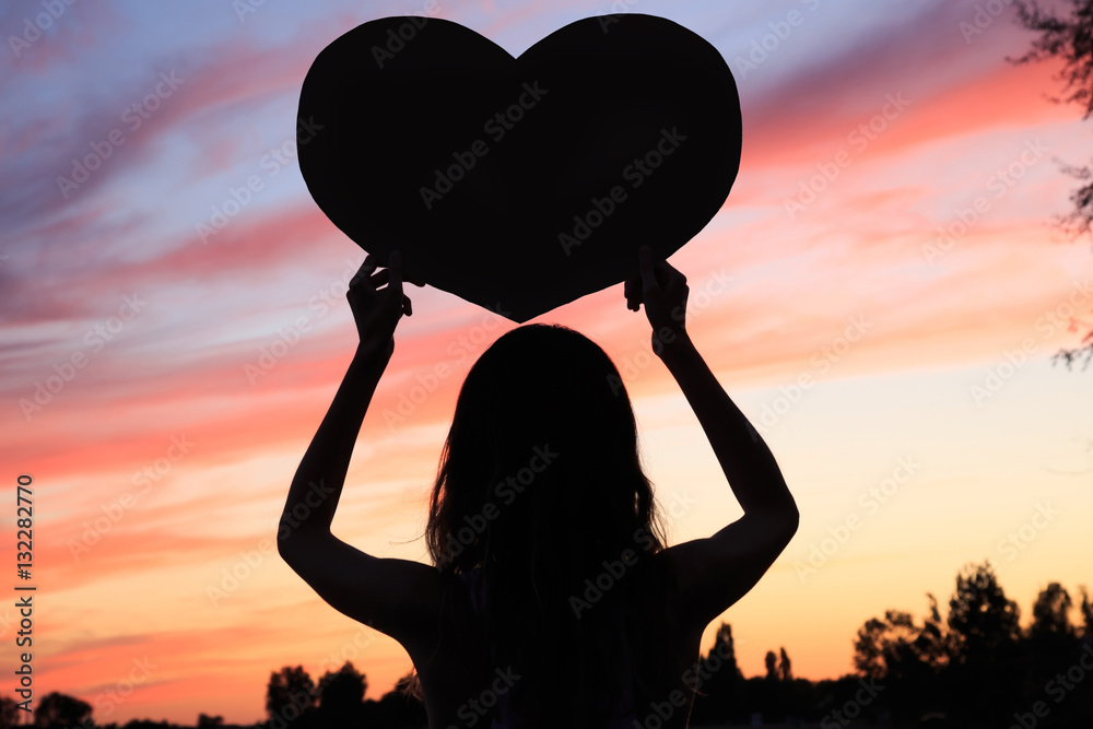 Female silhouette on sunset background with heart shape in hands