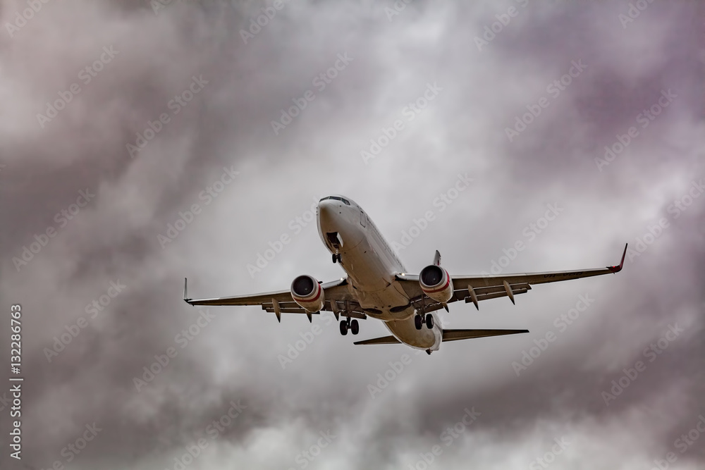 Passenger jet airplane low in the sky preparing to land with stormy clouds in the background