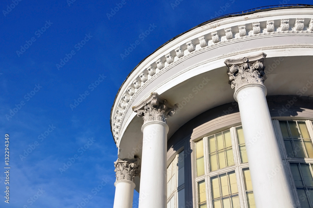 Looking up at a white round classical building with columns and capitals against the blue sky.