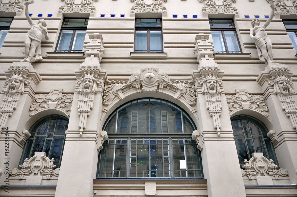 Looking up at the facade of old building with sculptures of human heads in Art Nouveau style (Jugendstil) and wide arched windows. Riga, Latvia.
