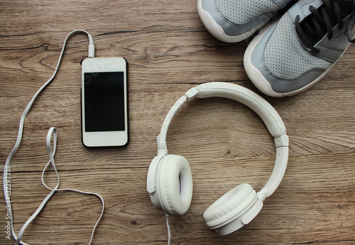 Sports kit for running: large white headphones, mobile phone, shoes on the wooden background