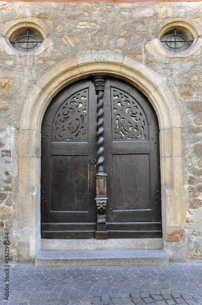 Arched wooden door of an old stone building with decorative carved elements. Kirchheim Teck, Baden-Wurttemberg, Germany.