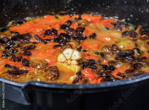 Pilaf on the cooking stage, zirvak with garlic, raisins, carrots, onions, lamb, barberry, saffron, zira and oil in a cauldron, boiling on the fire.