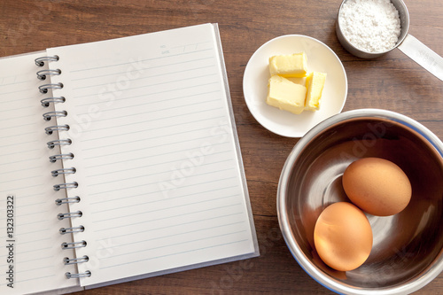 Obraz na płótnie Blank notebook with eggs, butter and flour in measure cup on the wooden table w salonie