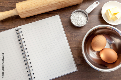 Blank notebook with eggs, butter, wood roller and flour in measure cup on the wooden table