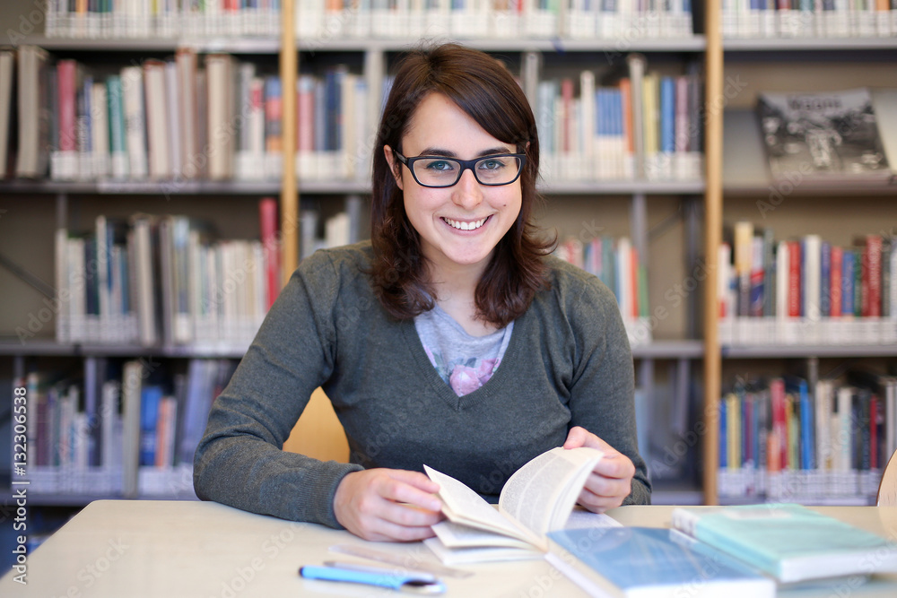long brown hair girl with black glasses studying and smiling in a library - portrait of pretty female student at work with books and pen on the desk long brown hair girl with black glasses studying and smiling in a library - portrait of pretty female student at work with books and pen on the desk
