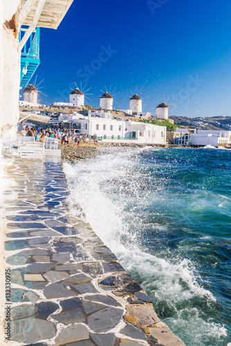 Splashing waves and famous Mykonos windmills in golden afternoon light, Mykonos island, Cyclades, Greece