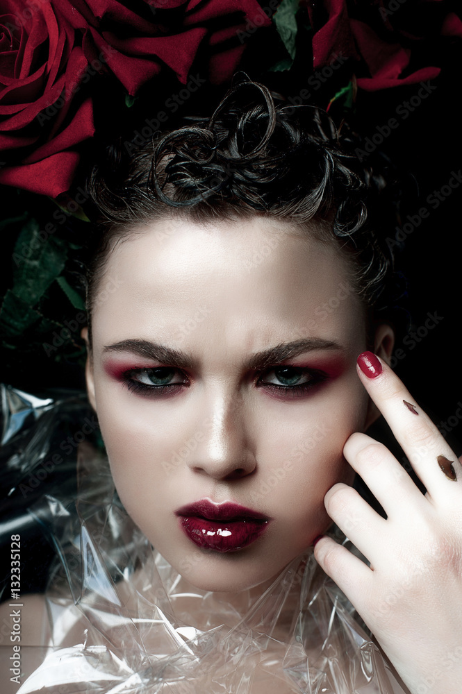 Fototapeta premium Beauty Fashion Model Woman face. Portrait with Red Rose flowers. Red Lips and Nails. Beautiful Brunette Woman with Luxury Makeup, perfect skin. Valentine.