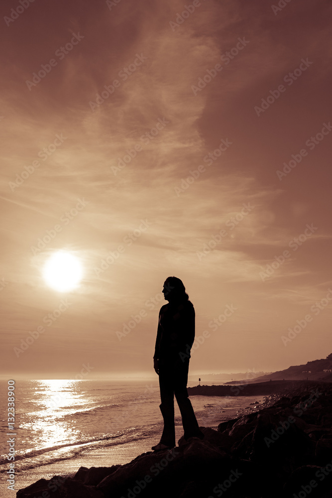 Silhouetted female figure stands on the coast at sunset