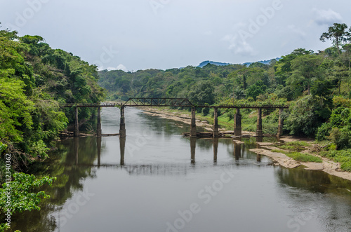 Crumbling iron and concrete walking bridge crossing large river in rain forest of Cameroon, Africa