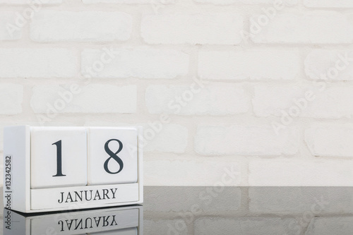 Closeup white wooden calendar with black 18 january word on black glass table and white brick wall textured background with copy space , selective focus at the calendar