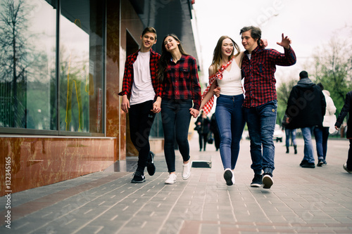 Four happy trendy teenage friends walking in the city, talking each other and smiling. Lifestyle, friendship and urban life concepts.