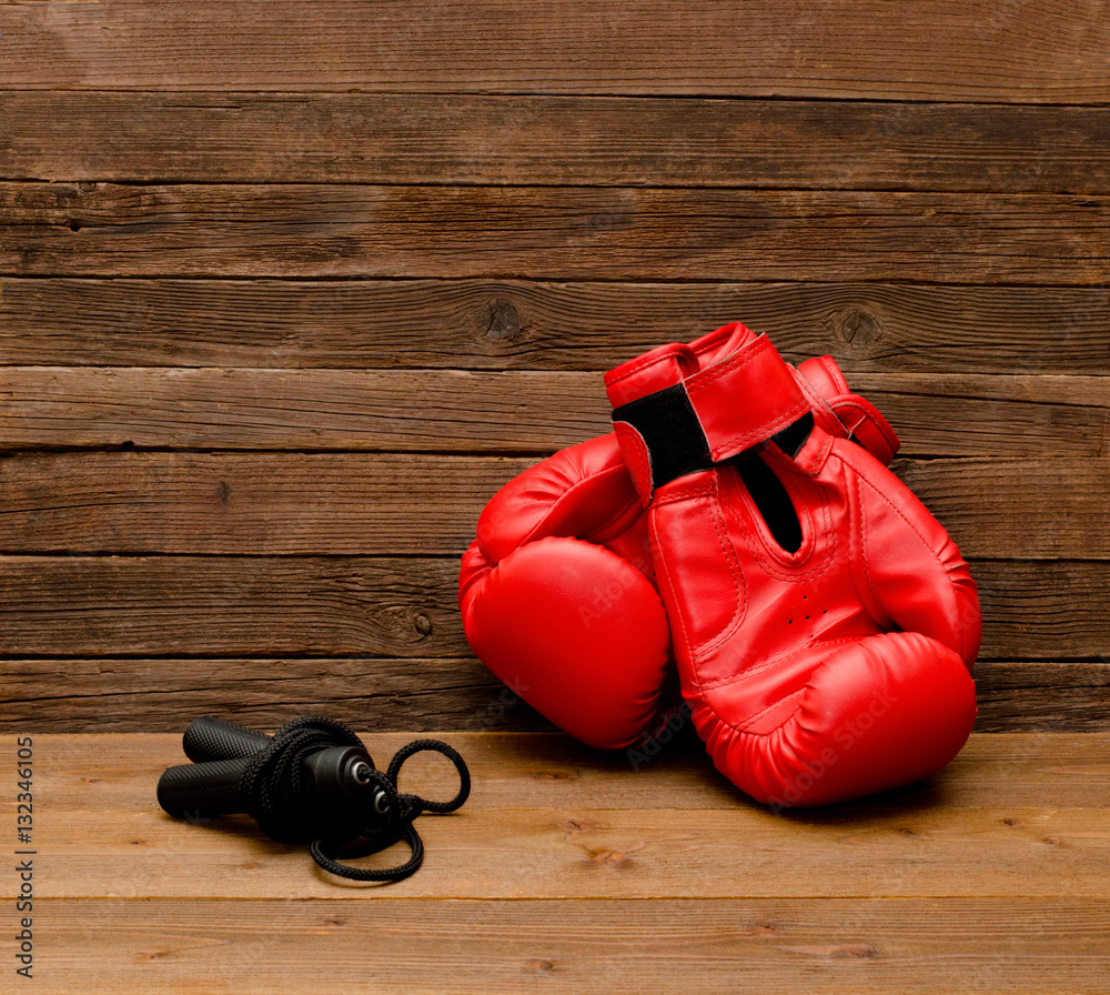 Two red boxing gloves lie on a wooden brown background, skipping rope empty space