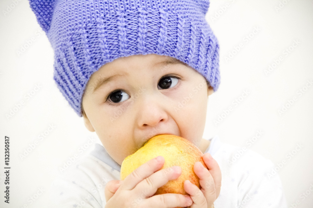 baby boy sitting on table with fruits and vegetables and eating an apple isolated on white background baby boy sitting on table with fruits and vegetables and eating an apple isolated on white background