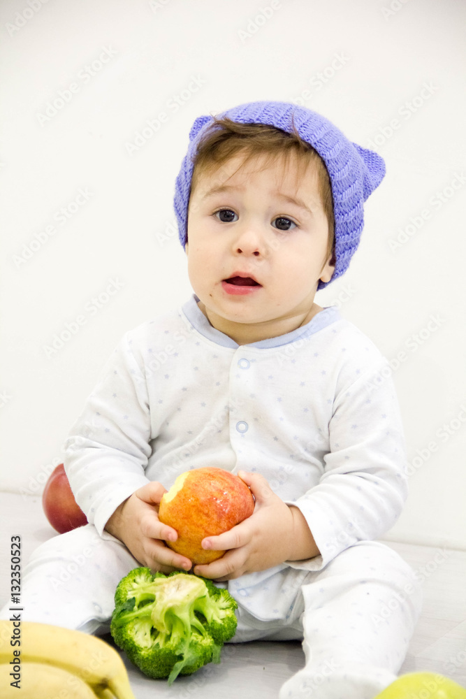Cute little caucasian boy 11 months old sits and eats red apple on white background Cute little caucasian boy 11 months old sits and eats red apple on white background