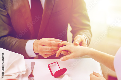 close up of man putting ring to his fiance finger