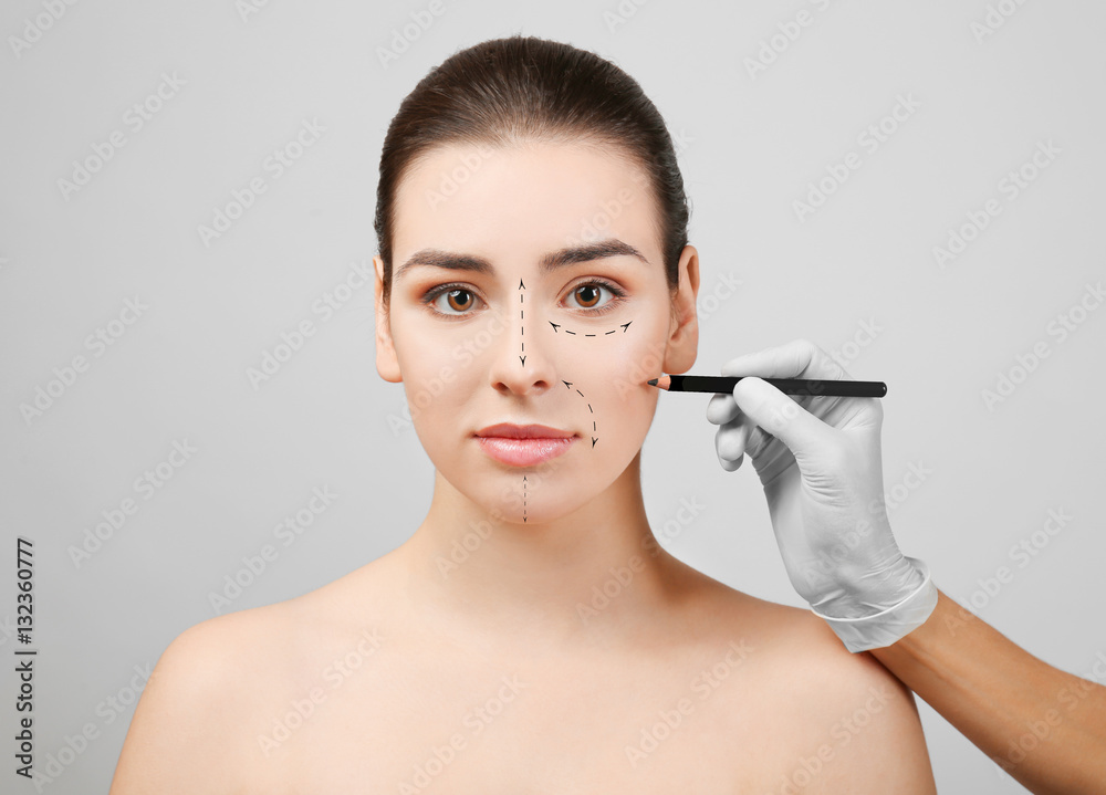 Plastic surgery concept. Doctor drawing marks on female face against gray background