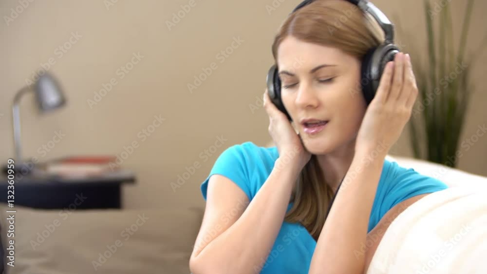Beautiful attractive young woman in a blue t-shirt sitting on sofa and listening to the music.