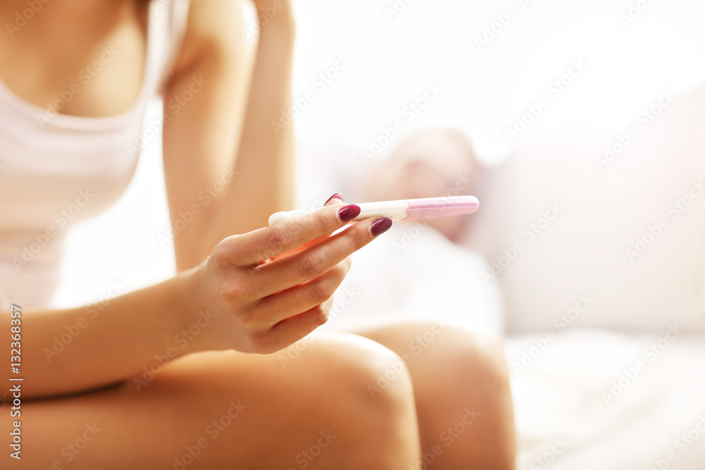 Woman with pregnancy test in bedroom - obrazy, fototapety, plakaty 