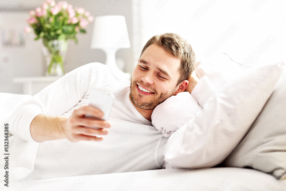 Handsome man lying in bed with smartphone Handsome man lying in bed with smartphone