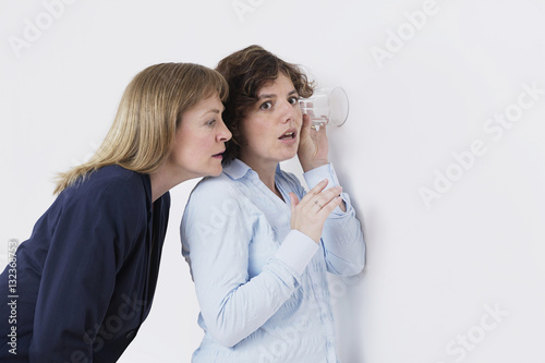 фотографія two women listening through wall with a glass