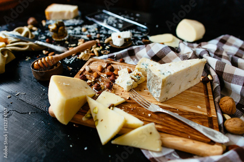 Assortment of cheese. Composition of different varieties of cheese with honey, nuts, olives on rustic dark wooden table