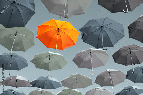 Concept of identity, character, personality and color. Bright orange outstanding  umbrella hanging among gray colorless umbrellas. 