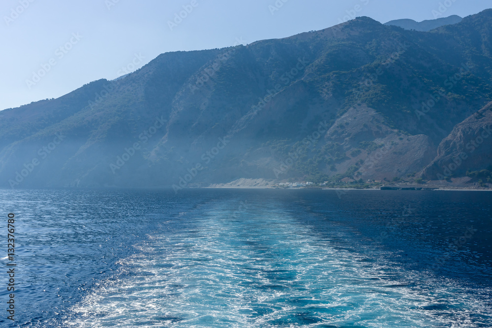 Mountains of southern coast of Crete. Waves (traces of movement) of the ship going in the distance.