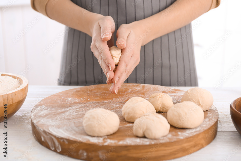 Woman making buns from raw dough on kitchen table
