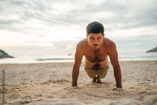 Sports and lifestyle. Man doing push-ups or plank on the beach. Male athlete exercising outdoors.