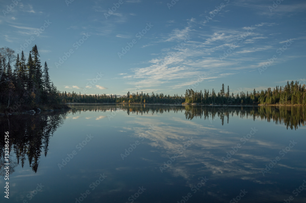 Still Northern Ontario lake in early morning with reflected clou