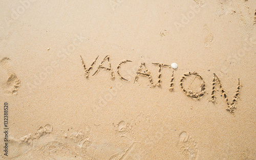 VACATION message written on the sand beach with human footprint