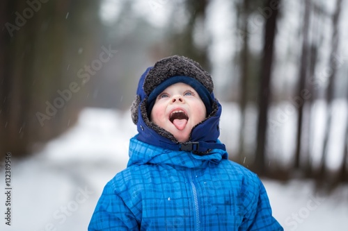 Happy little boy playing outdoor in winter snow. Boy catching snow with his tongue